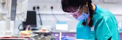 A female dental student wearing a face mask working on a phantom head.