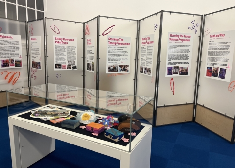 A view of the exhibition space with the current exhibition 'Storming the Teacup'. In the foreground is a display case with various items in, and in the background are display boards