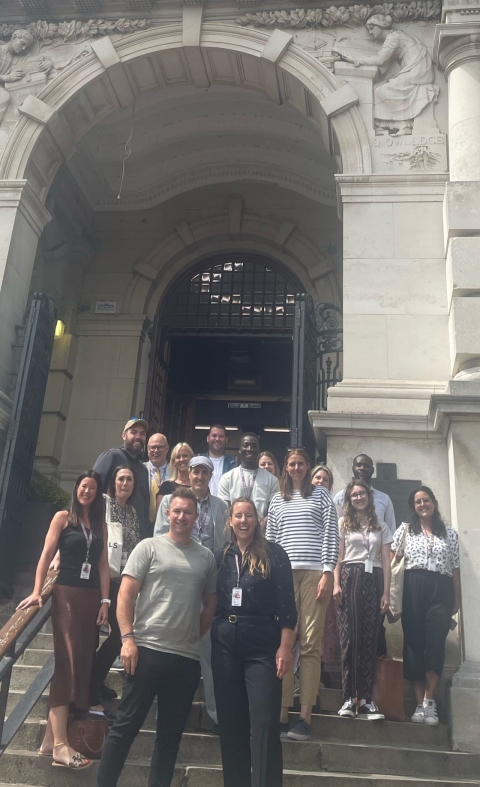 A group of people standing together on the steps of a building, engaged in conversation and enjoying the outdoors.
