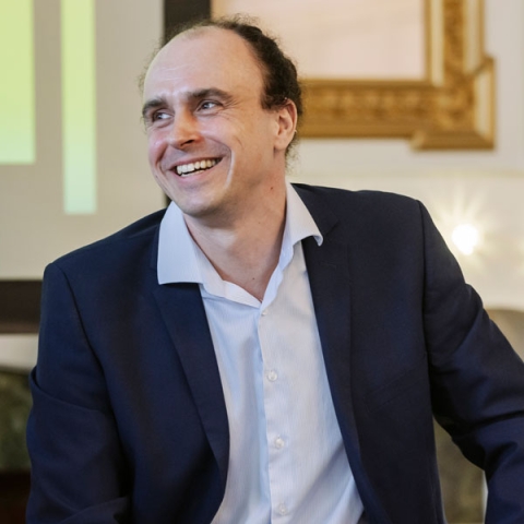 Image of alumnus Graham Edmunds laughing on camera wearing shirt and jacket