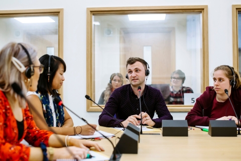 Group of students in headsets sit around table in interpreter suite