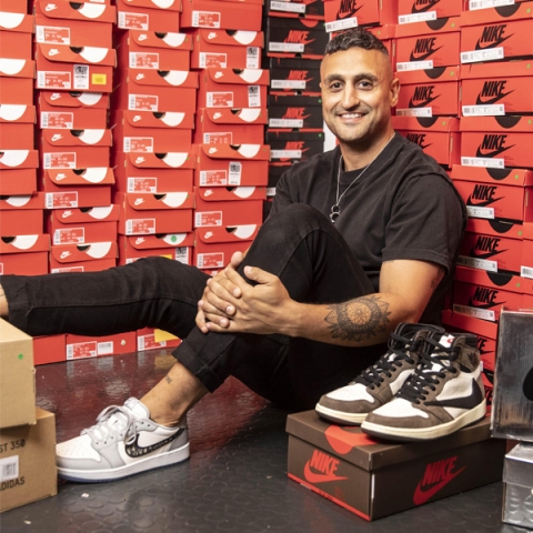 Image of Moses Rashid sat on floor in black tshirt and jeans surrounded by trainer boxes