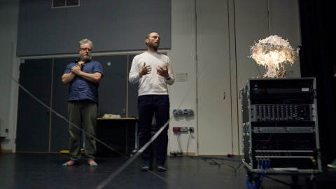 Two people standing with a paper model of the mushroom cloud during a performance for the event