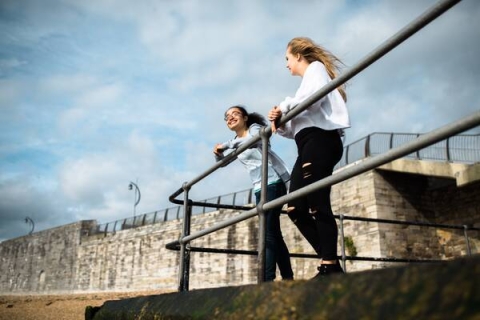 Two students leaning against barriers that look over the sea, laughing