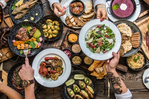 People reaching for plates of food surrounded by a table busy with dishes of food