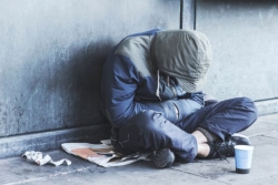 Homeless person sitting on sidewalk with head down