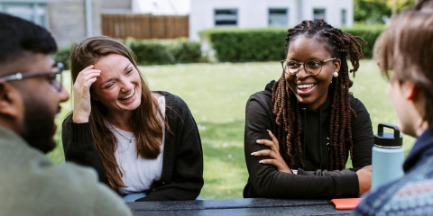 Students smiling in sun at picnic table outside of the Students' Union