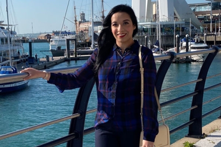 Ahsana wearing shirt and jeans with bag over shoulder in front of marina at Gunwharf Quays