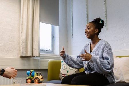 A woman sat speaking to another person, with a table in between them with a toy on it.