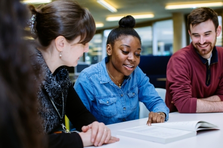 Staff member talking to two students at a table, supporting them with some of their work