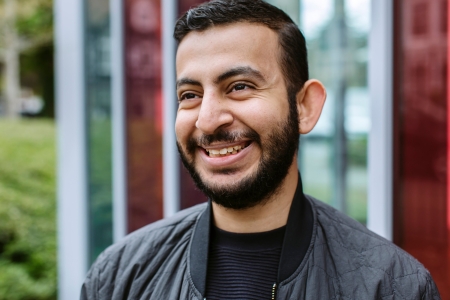 Headshot of male student stood outside glass university building smiling