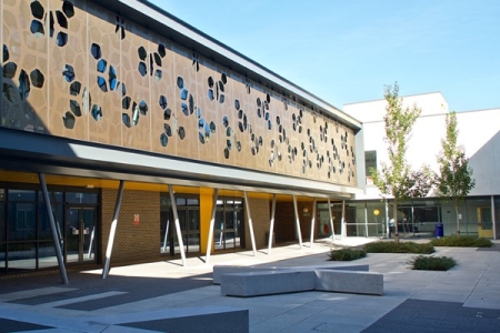 A modern building with decorative cladding and paved courtyard with seating, part of Eastleigh College